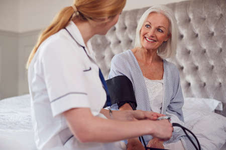 Female Doctor Making Home Visit To Senior Woman In Bedroom For Blood Pressure Checkの写真素材