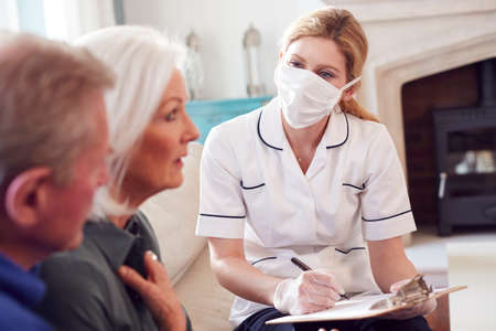 Female Doctor With Mask Makes Home Visit To Senior Couple For Medical Check During Covid-19 Lockdownの写真素材