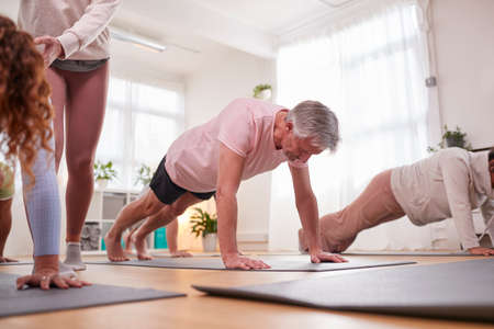 Teacher Helping Group Stretching On Exercise Mats In Yoga Or Fitness Class Inside Community Center