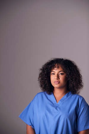 Studio Portrait Of Female Nurse Wearing Scrubs Standing Against Grey Backgroundの写真素材