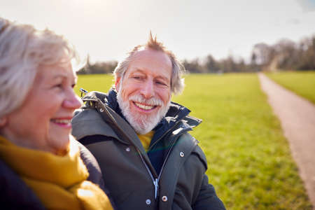 Loving Senior Couple Sitting On Seat Enjoying Autumn Or Winter Walk Through Park Togetherの写真素材