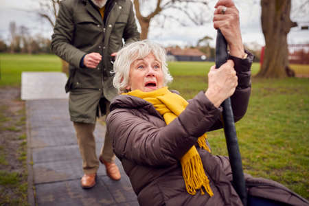 Senior Couple Having Fun Playing On Swing In Park Playground