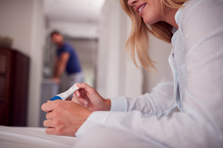 Close Up Of Smiling Woman Wearing Pyjamas In Bedroom Holding Positive Pregnancy Test