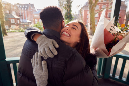 Romantic Man Hugging Young Woman After Giving Her Bouquet Of Flowers As They Meet In City Parkの写真素材