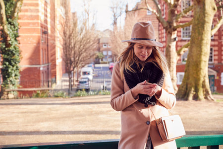 Woman In City Park Waiting For Date To Arrive Sends Text Message On Mobile Phoneの写真素材