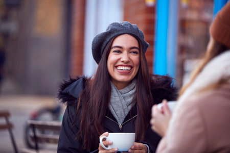 Two Female Friends Meeting Sitting Outside Coffee Shop On City High Streetの写真素材