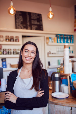 Portrait Of Smiling Female Owner Of Coffee Shop Standing Behind Counterの写真素材