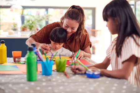 Asian Mother With Children Having Fun With Children Doing Craft On Table At Homeの写真素材