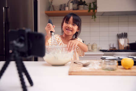 Asian Girl Baking Cupcakes In Kitchen At Home Whilst On Vlogging On Mobile Phoneの写真素材