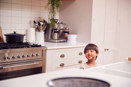 Smiling Young Asian Boy Standing In Kitchen At Homeの写真素材