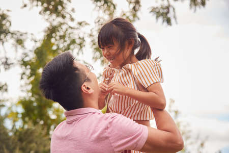 Asian Father Lifting Daughter In Mid Air As They Play Game In Garden Togetherの写真素材