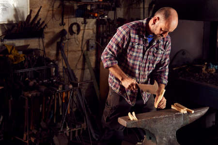 Male Blacksmith Chopping Wood For Kindling On Anvil To Light Forge