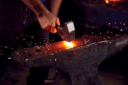 Close Up Of Male Blacksmith Hammering Metalwork On Anvil With Sparksの写真素材