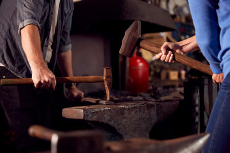 Close Up Of Two Blacksmiths Hammering Metalwork On Anvilの写真素材