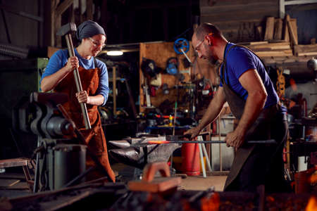 Male And Female Blacksmiths Hammering Metalwork On Anvil With Sparks