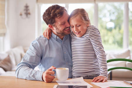 Loving Daughter At Home With Father Sitting At Table With Paperworkの写真素材
