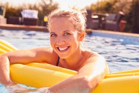 Portrait Of Woman Having Fun With Inflatable On Summer Vacation In Outdoor Swimming Pool