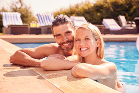 Portrait Of Couple Having Fun On Summer Vacation Relaxing In Outdoor Swimming Pool