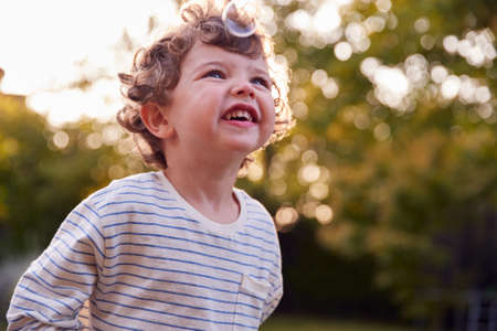 Young Boy Having Fun In Garden Chasing And Bursting Bubblesの写真素材