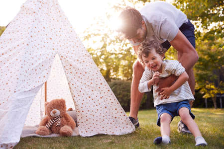 Father And Son Having Fun With Tent Or Tepee Pitched In Gardenの写真素材