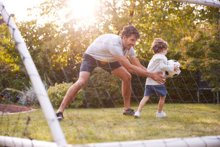 Father With Son Having Fun In Park Or Garden Playing Soccer Together