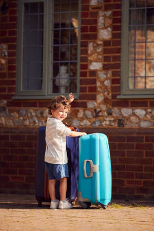 Young Boy With Suitcase Outside House Preparing To Leave For Family Vacationの写真素材