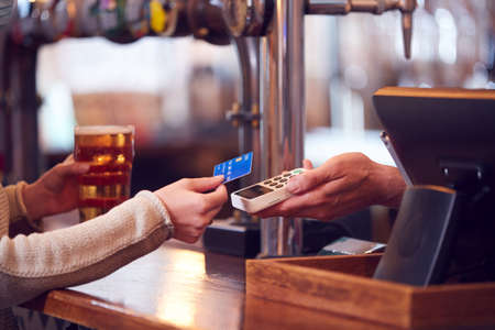 Close Up Of Female Customer In Bar Making Contactless Payment With Card For Drinks To Male Bartenderの写真素材
