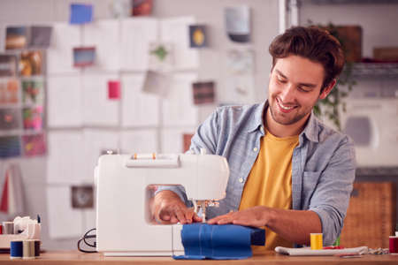 Smiling Male Student Or Business Owner Working In Fashion Using Sewing Machine In Studioの写真素材