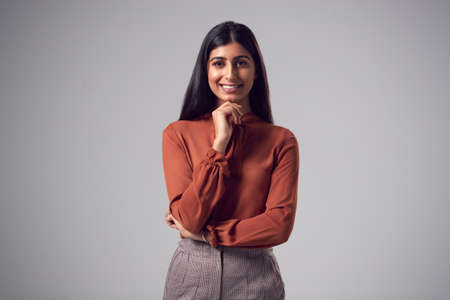 Studio Portrait Of Smiling Young Businesswoman With Chin Resting On Hand Against Plain Backgroundの写真素材