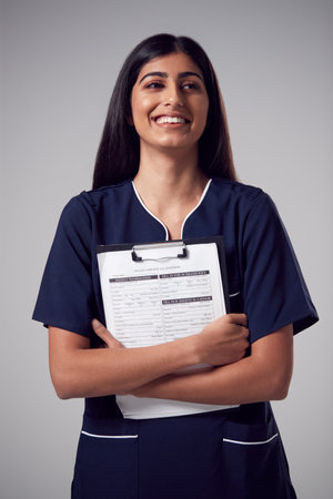 Studio Portrait Of Smiling Female Nurse With Clipboard Wearing Uniform Against Plain Backgroundの写真素材
