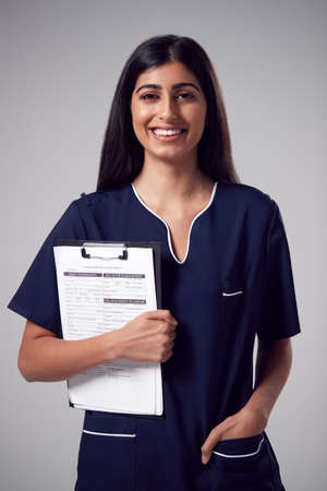 Studio Portrait Of Smiling Female Nurse With Clipboard Wearing Uniform Against Plain Backgroundの写真素材