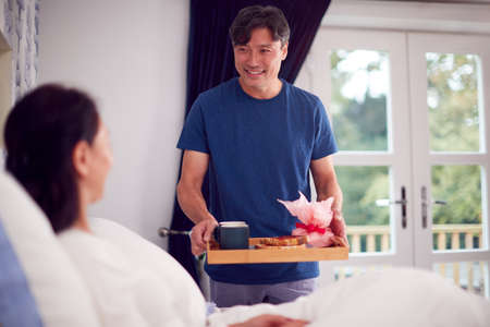Mature Asian Man Bringing Wife Breakfast In Bed To Celebrate Birthday Or Anniversaryの写真素材