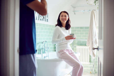 Mature Asian Couple Wearing Pyjamas Sitting In Bathroom Enjoying Morning Hot Drinks Togetherの写真素材