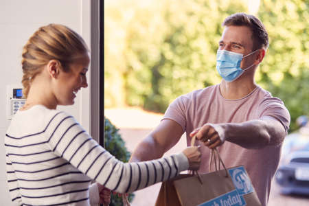 Man Wearing Mask Making Home Delivery Of Takeaway Food To Front Door Of House During Health Pandemic