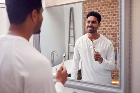 Man Wearing Pyjamas At Home In Modern Bathroom Brushing Teeth In Mirrorの写真素材
