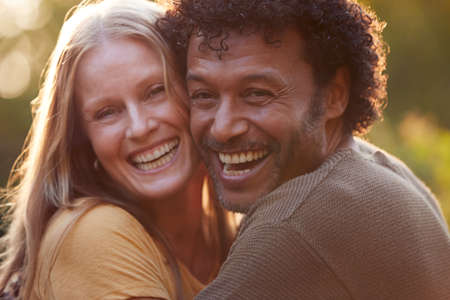 Portrait Of Loving Mature Couple Hugging Outdoors Against Flaring Evening Sunの写真素材
