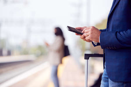 Close Up Of Businessman On Railway Platform Texting On Mobile Phoneの写真素材