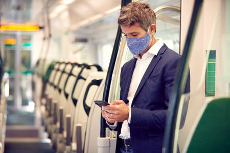 Businessman Stands In Train Carriage Using Mobile Phone Wearing PPE Face Masks During Pandemicの写真素材