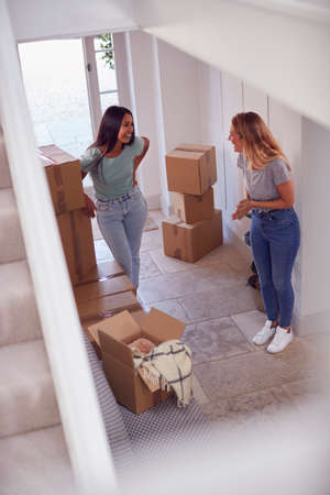 Excited Female Couple Carrying Boxes Through Front Door Of New Home On Moving Dayの写真素材