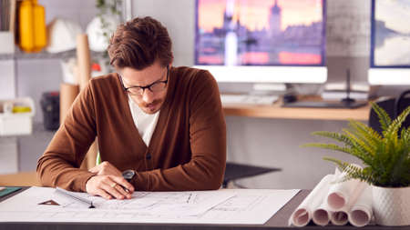 Male Architect In Office Working At Desk Studying Building Plansの写真素材