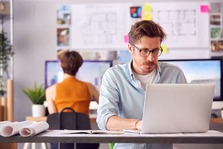 Male And Female Architects In Office Working At Desk On Laptop And Desktop Computers