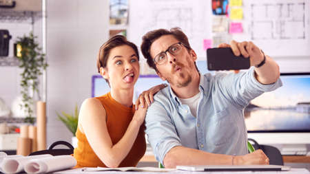 Male And Female Architects In Office Posing For Selfie And Pulling Funny Faces Together