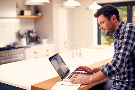 Man Working From Home Using Laptop On Kitchen Counterの写真素材