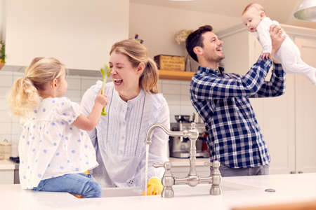 Smiling Family Having Fun In Kitchen Doing Washing Up At Sink Together