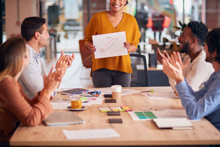 Colleagues Applauding As Businesswoman Gives Presentation In Modern Open Plan Officeの写真素材