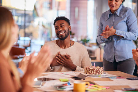 Colleagues Celebrating Businessman's Birthday At Meeting Around Table In Modern Open Plan Officeの写真素材