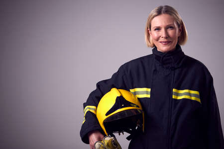 Studio Portrait Of Smiling Mature Female Firefighter Holding Helmet Against Plain Backgroundの写真素材
