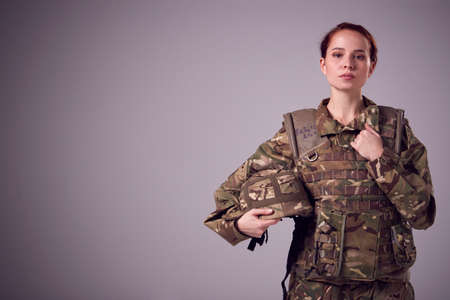 Studio Portrait Of Serious Young Female Soldier In Military Uniform Against Plain Backgroundの写真素材