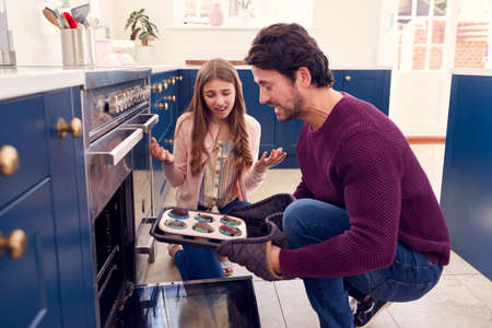 Father With Teenage Daughter Taking Out Burnt Homemade Cupcakes From The Ovenの写真素材