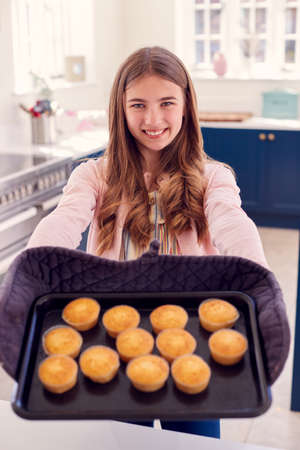 Portrait Of Proud Teenage Girl Taking Out Tray Of Homemade Cupcakes From The Oven At Homeの写真素材